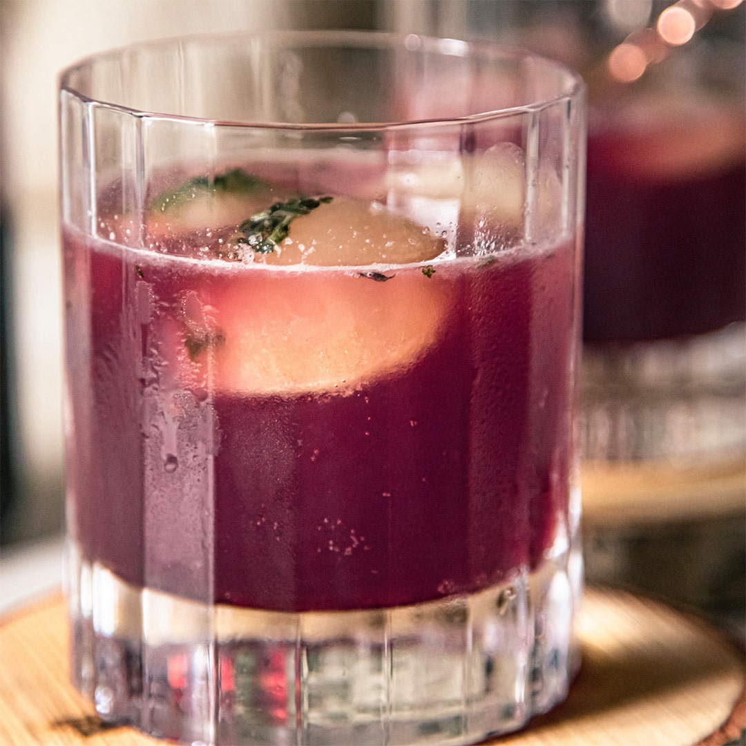 Clear glass with layered drink and fruit on a wooden coaster